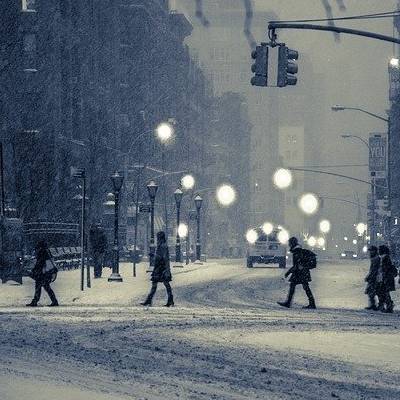 People crossing snowy street in dimly lit city.